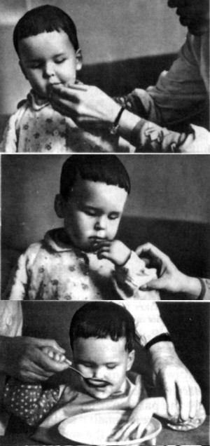 Instructing a deaf-blind child in the gesture denoting eatThe girl reproduces the gesture with some help from the teacherTeaching the girl to hold the spoon and lift it to her mouth